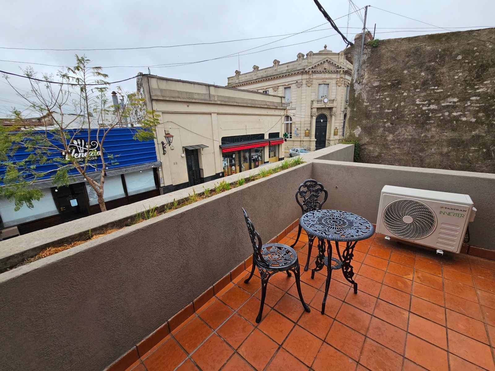Balcón privado con mesa y sillas de hierro, con vista a la calle