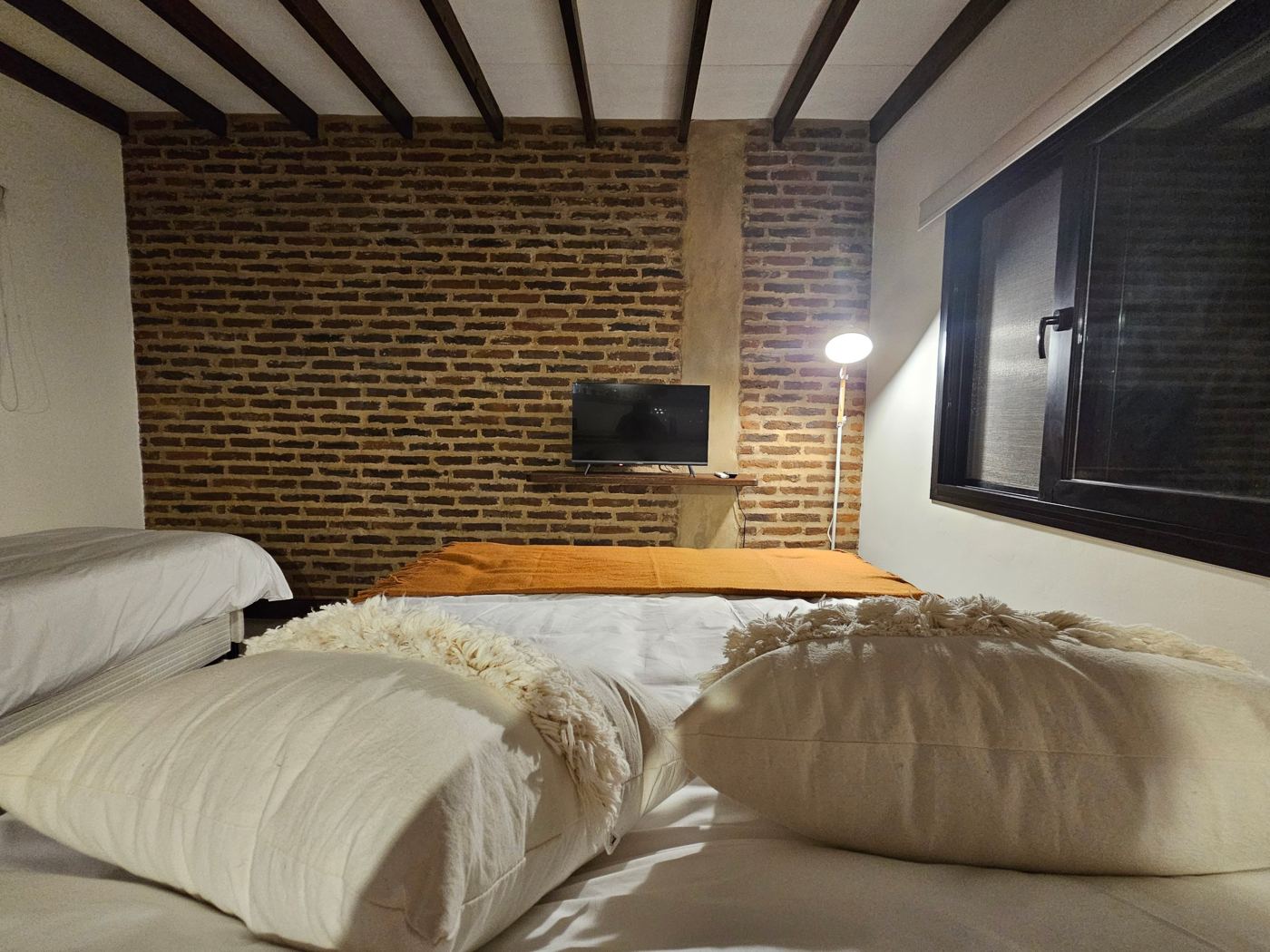 Cama matrimonial frente a la pared de ladrillo