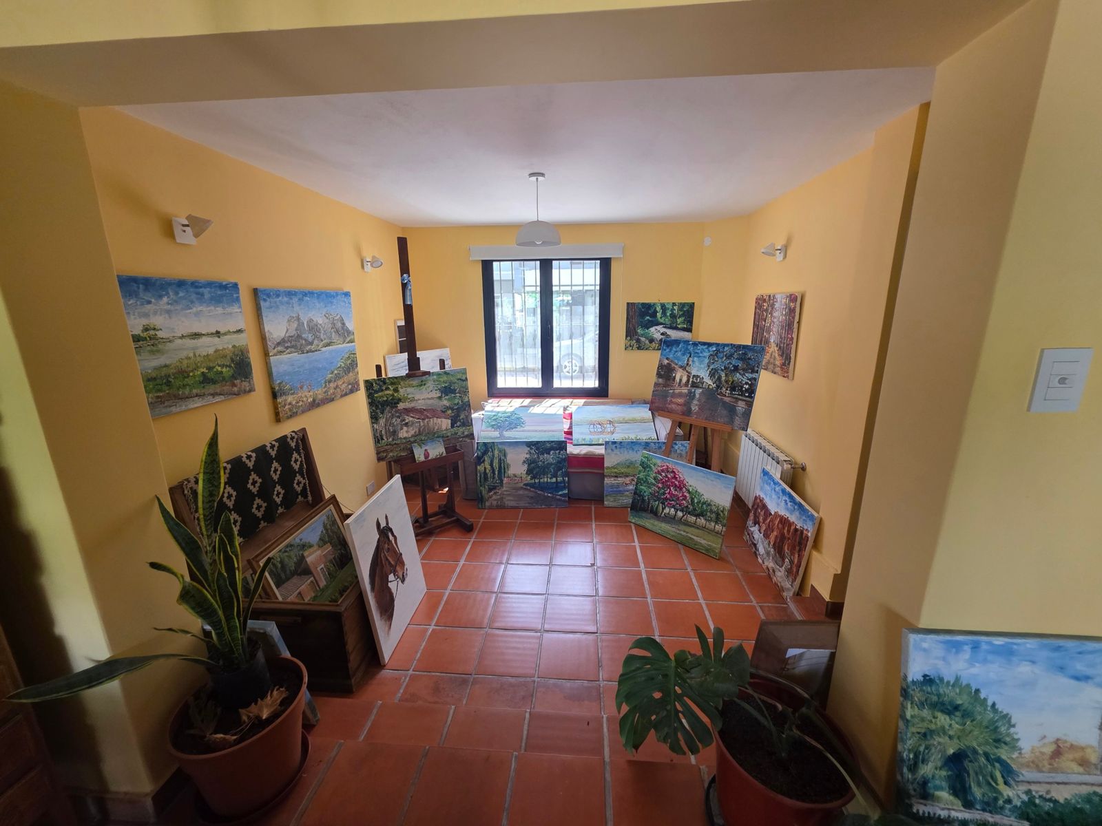 Sala del atelier con paredes amarillas y cuadros apoyados en el piso de baldosa