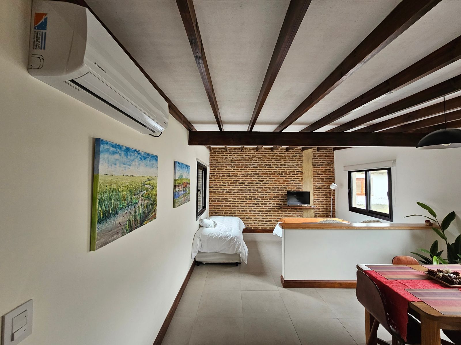 Ambiente amplio con pared de ladrillo, camas y comedor con mantel rojo